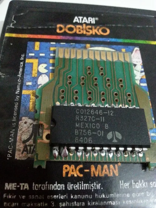 A photo showing the PCB and ROM chip of a Pac-Man cartridge manufactured in Turkey. One can see something unusual about two adjacent pins leading from the ROM to the PCB.